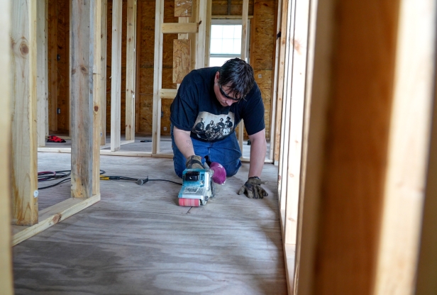 A man using a belt sander on the floor of a building being constructed.
