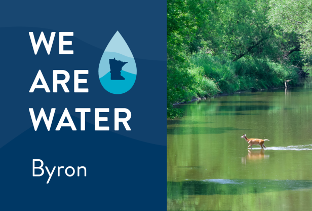 We Are Water Byron. A deer crossing a wide, shallow river lined with trees. 