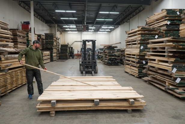 A man adds a board to a stack on a pallet in a warehouse. 