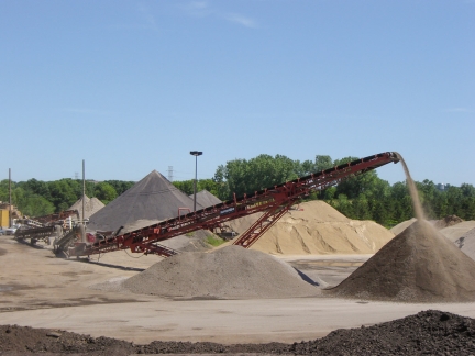 A red conveyor belt pours gravel on top of a large mound.