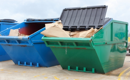Blue and green commercial waste dumpsters filled with cardboard.