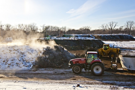 A red tractor drives by a large pile of steaming compost.