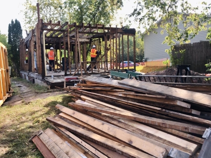 Pile of boards recovered from home that workers are deconstructing in background.