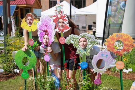 Group of girls place their faces in flower cut outs to have photo taken.