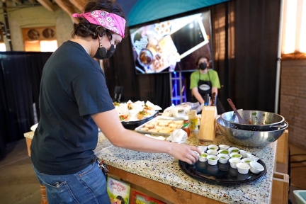 A person places samples of food in small white paper cups on a tray.