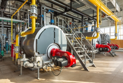 An industrial boiler room with three large boilers, many pipes and valves.