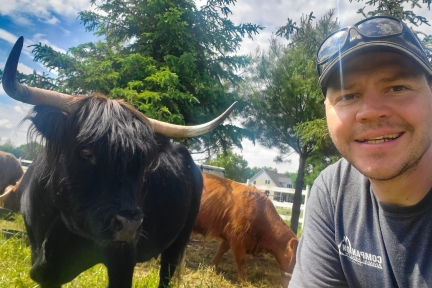 A selfie of a smiling man and a black Scottish Highland cow.