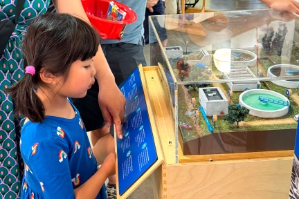 A young girl looking at a scale model of a wastewater treatment plant. 