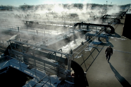 Man walking by wastewater treatment tanks with steam rising from the water
