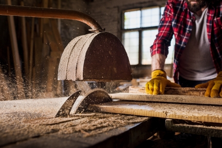 Carpenter in protective gloves sawing boards at sawmill.