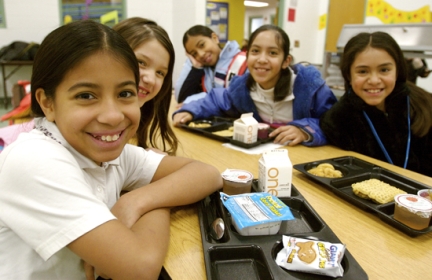 Smiling school kids with lunch trays sit around a table.
