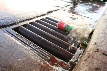 Water rushing into storm drain carrying a paper cup and other debris.