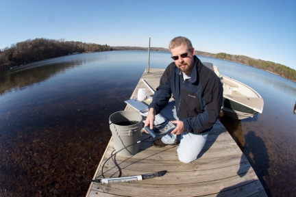 Man kneeling on dock with bucket and other water monitoring equipment