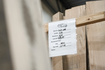 White plastic tag attached to lumber listing species of wood, grade, thickness, city, and zip code of origin.