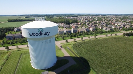 White water tower next to cornfield and suburban neighborhood.