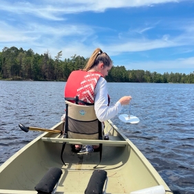 Waverly Reibel in a canoe holding a Secchi disk above the water.