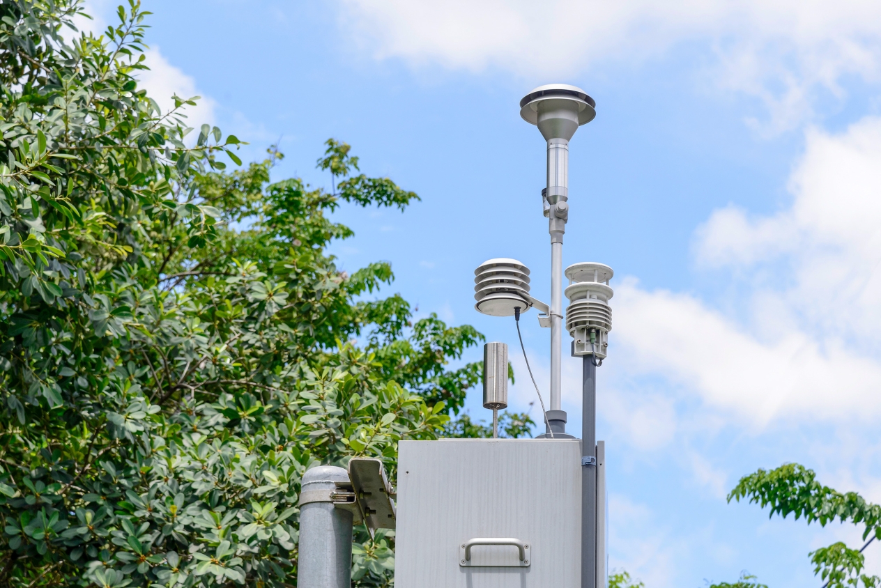 A metal box with saucer-shaped collection instruments on poles attached to the top with trees and blue sky in the background.