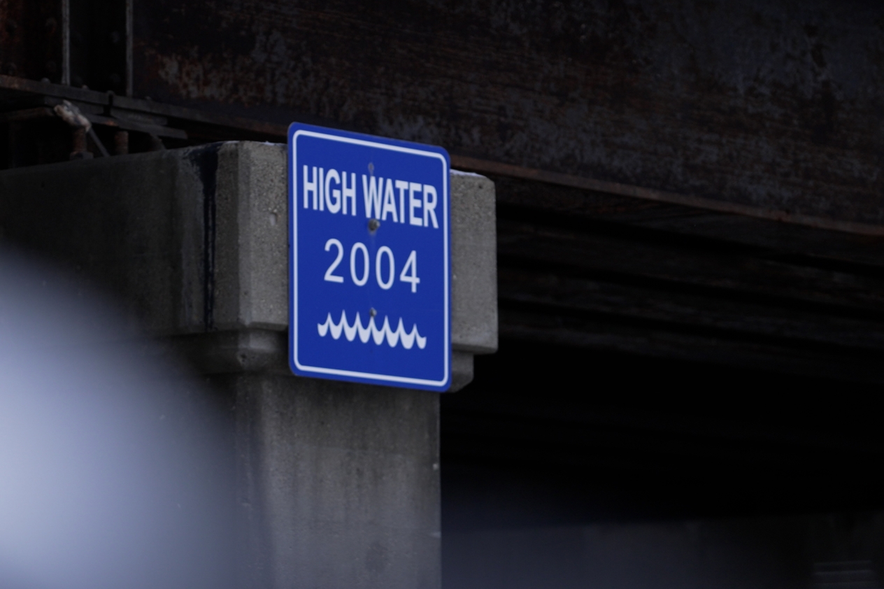 A blue sign with white wave symbol on a bridge support that says "High water 2004."