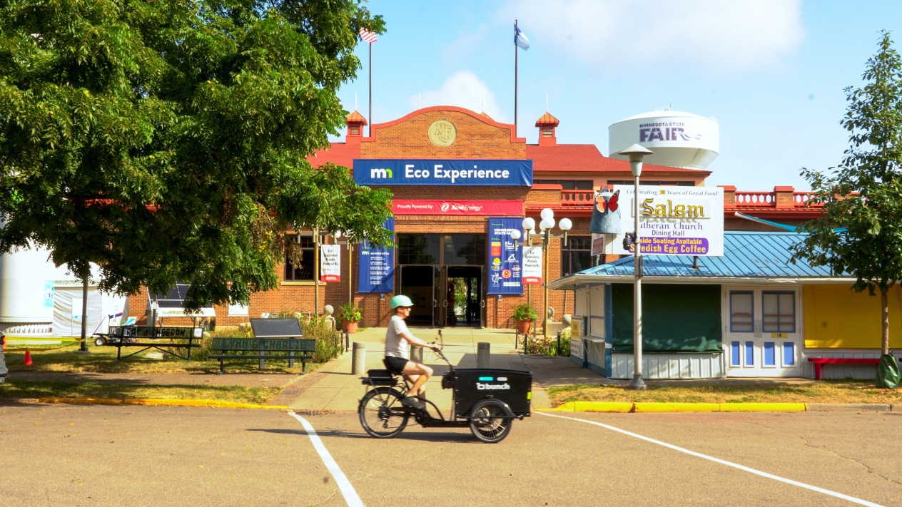 A person riding a cargo e-bike in front of the Eco Experience building at the Minnesota State Fair