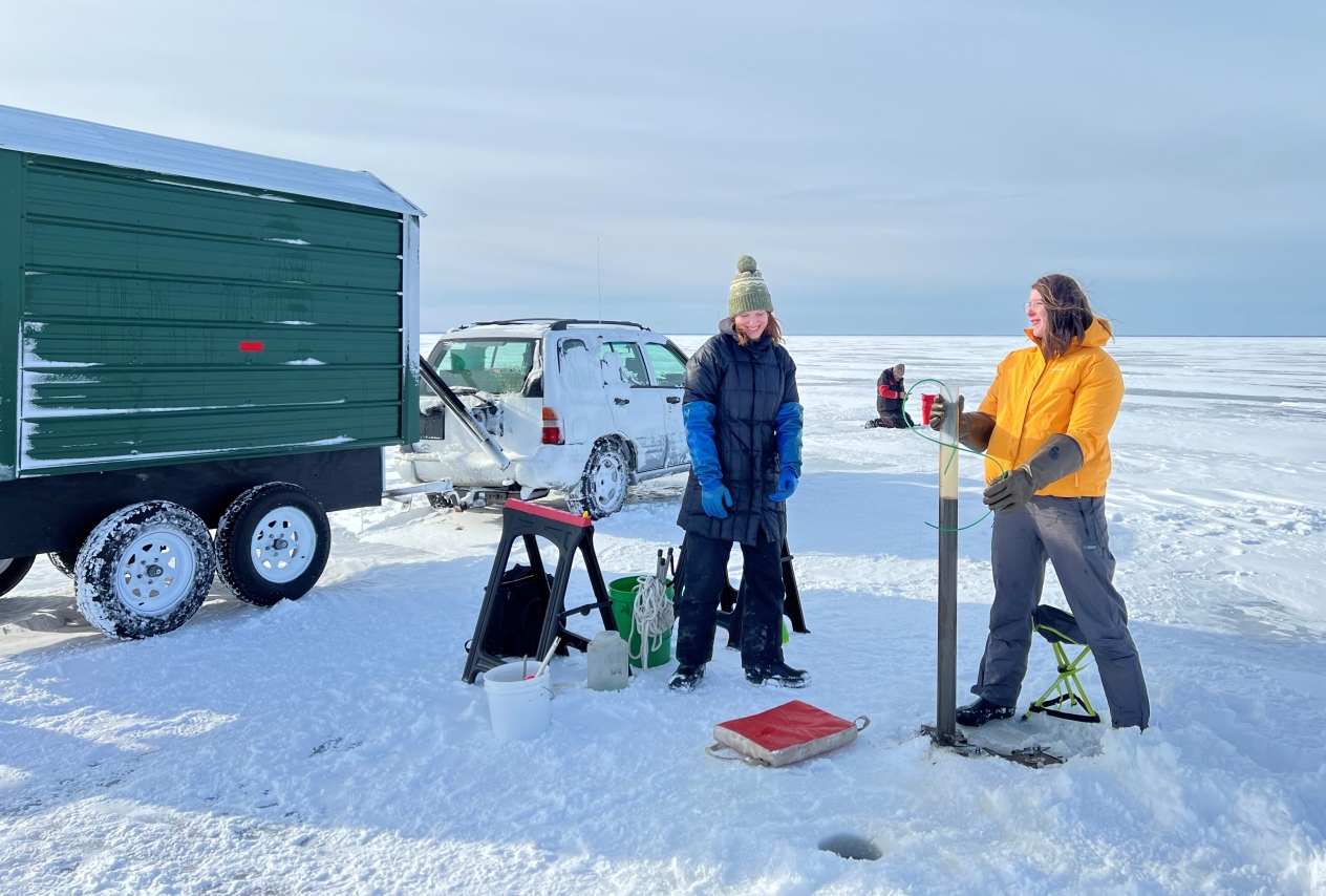Researchers standing on a frozen lake and collecting samples of sediment from the bottom of the lake