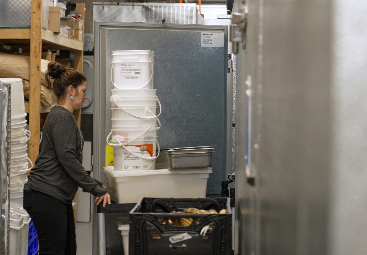 Woman pushing a cart loaded with buckets into a walk in freezer.