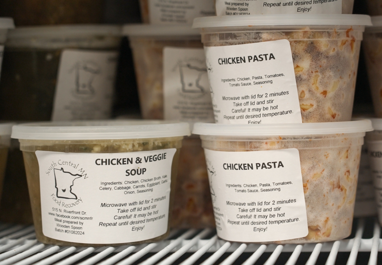 Plastic food containers in refrigerator labeled "chicken & veggie soup" and "chicken pasta". 