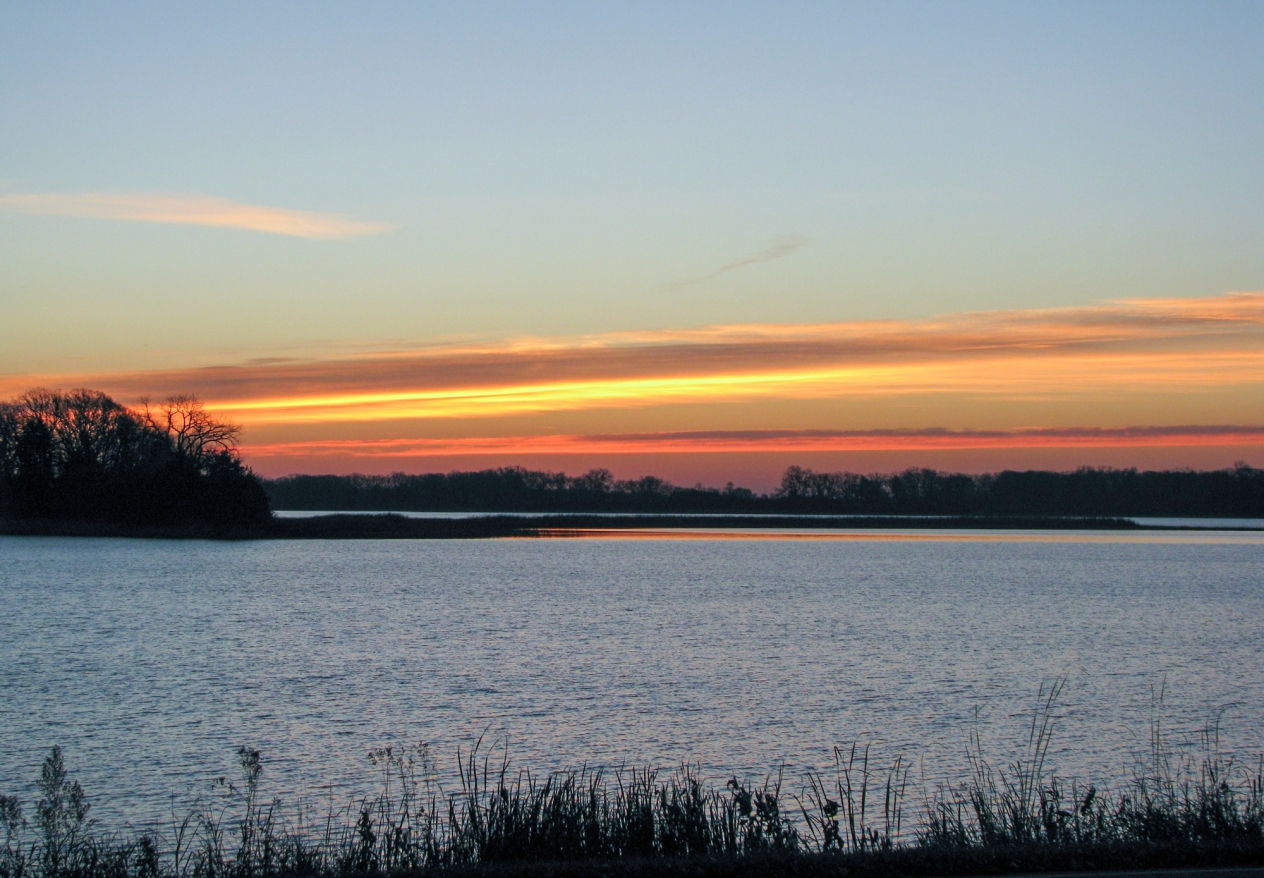 Clouds reflect an orange sunset over a blue lake.