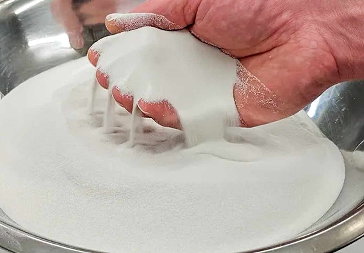 Close up of a hand holding a scoop of glass beads the size of sand.