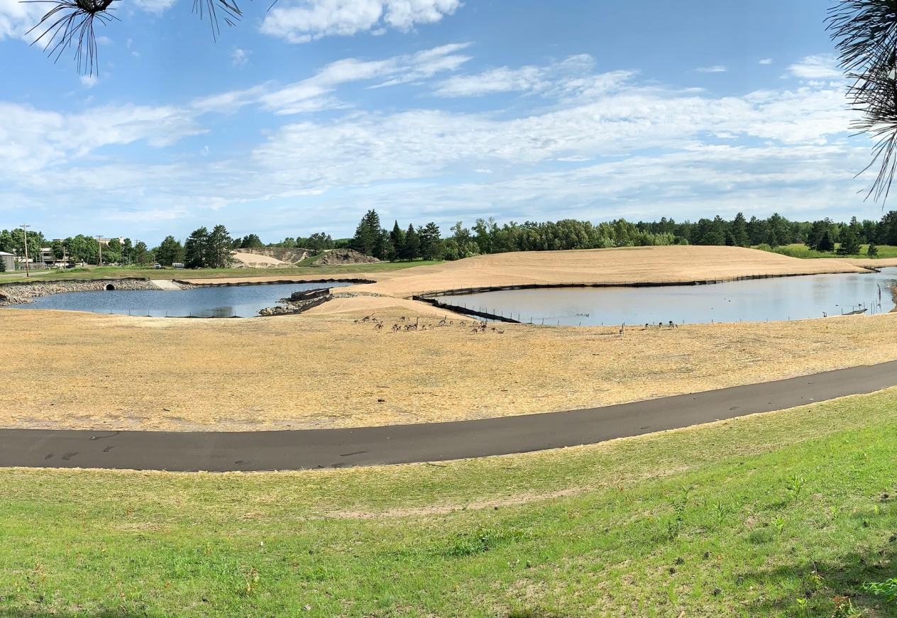 Wide angle of stormwater ponds surrounded by newly seeded soil and erosion control with a walking path in the foreground.