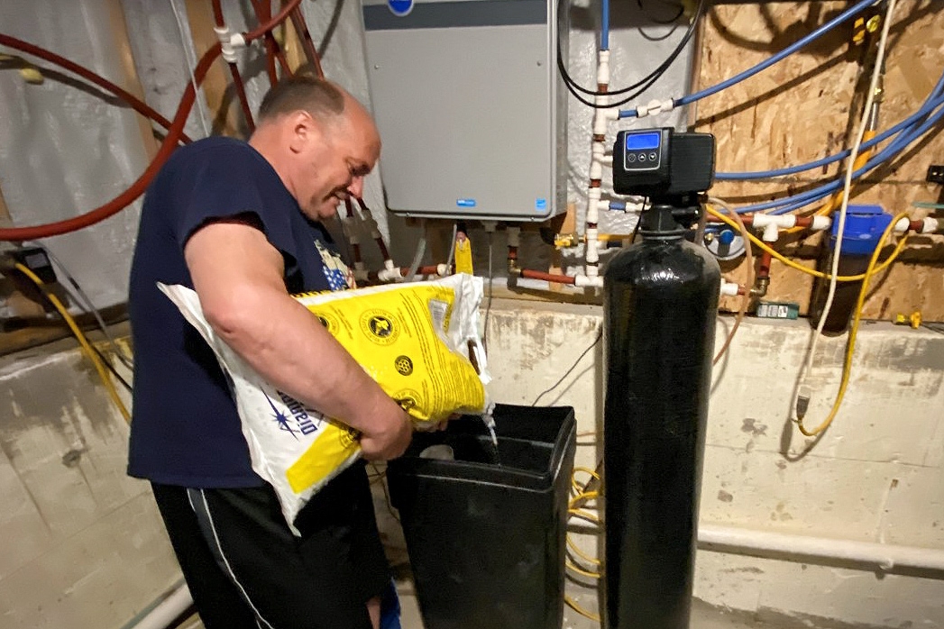 Man pours salt into water softener system in basement.
