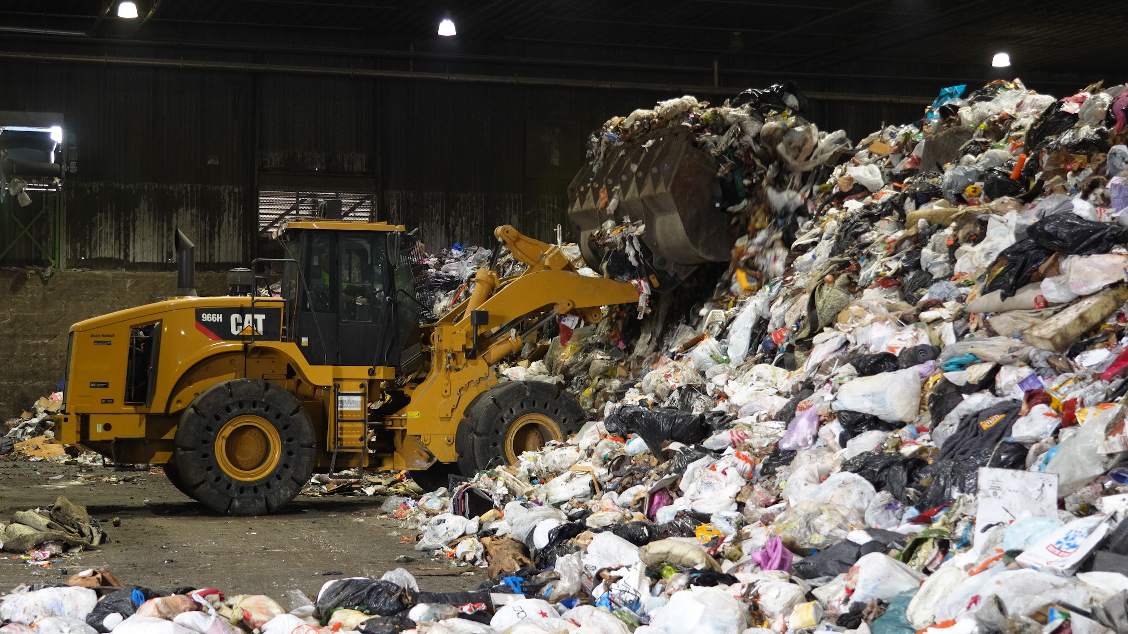 A front-end loader moves piles of bagged trash at a waste facility